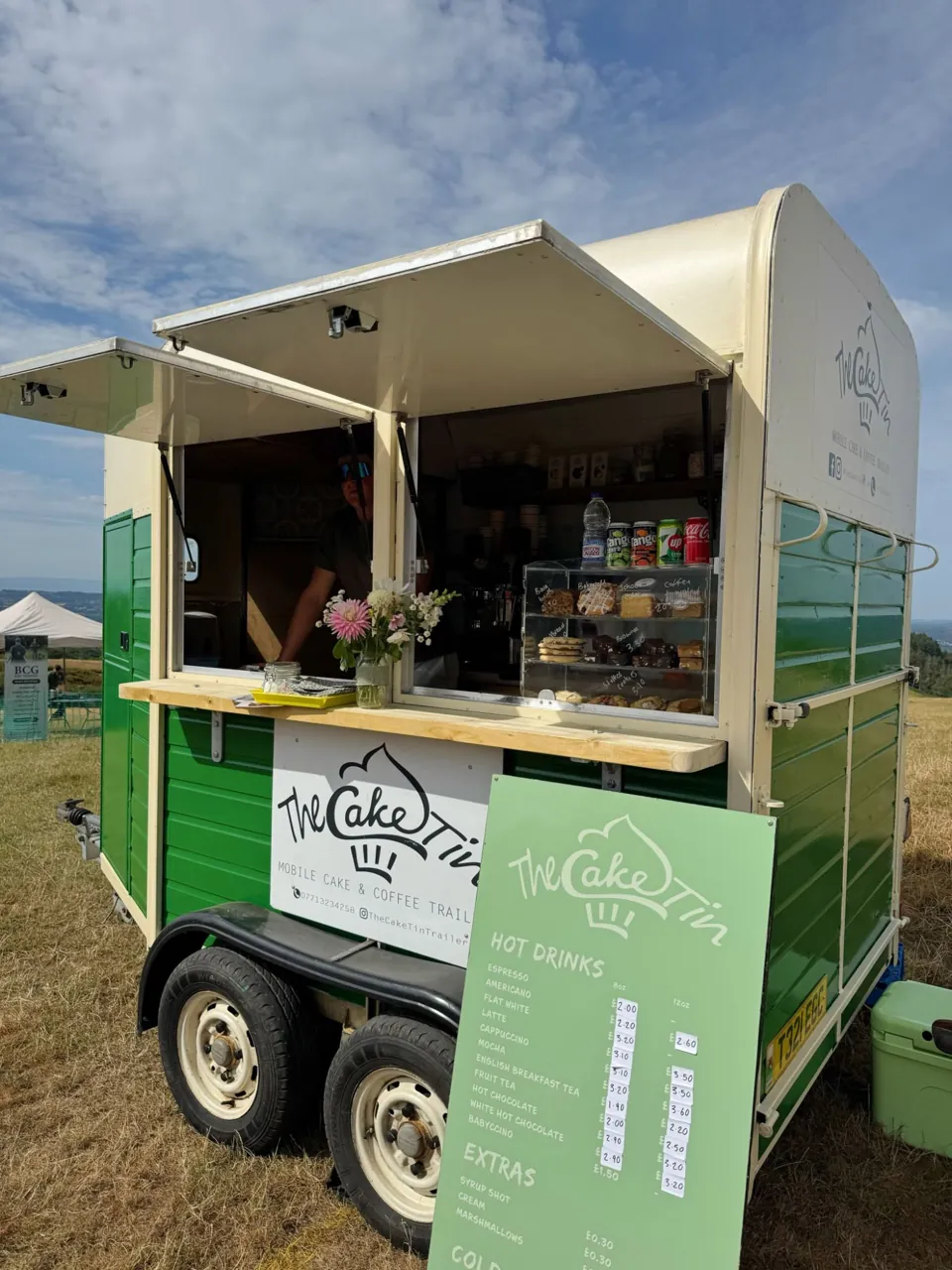 The green Cake Tin trailer open at a hilltop event with its menu board