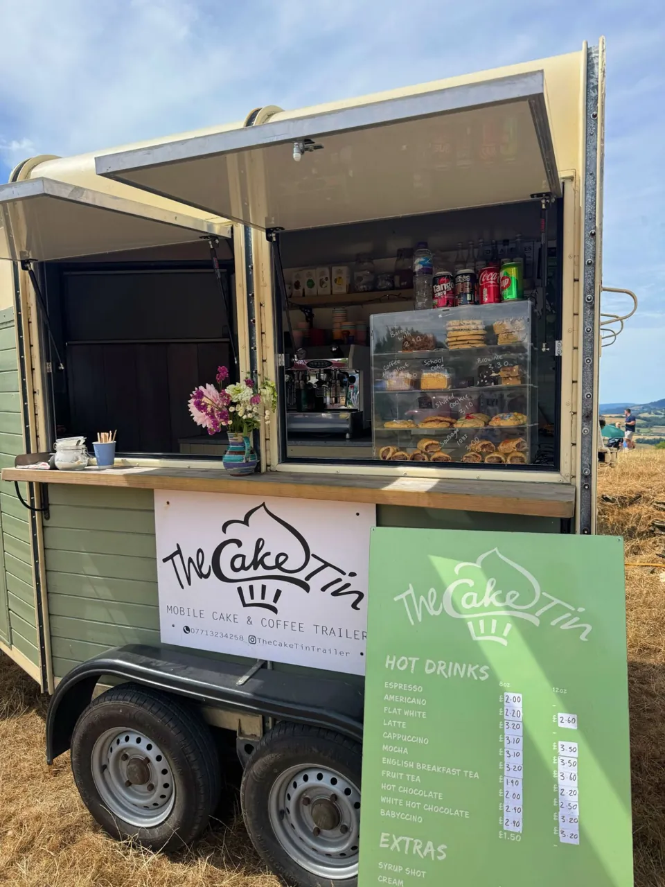 The sage Cake Tin trailer with its hatches open, a coffee machine and a cabinet of homemade bakes