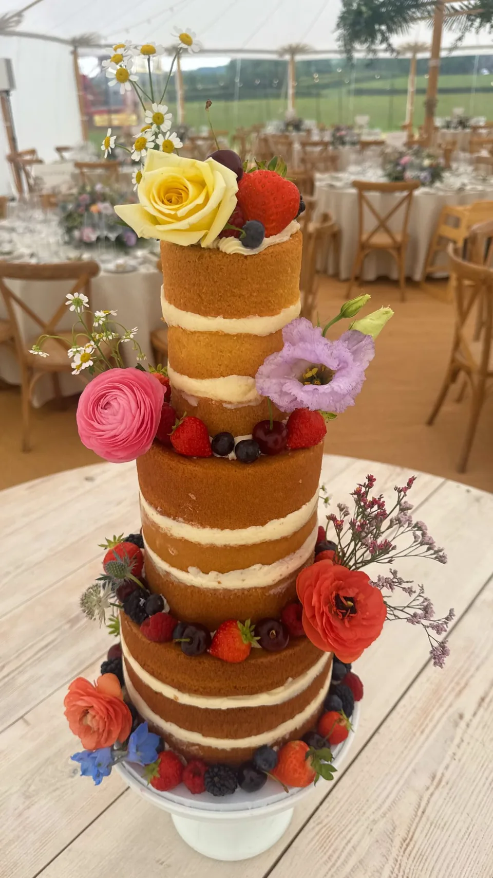 A three-tier wedding cake with fruit and fresh flowers